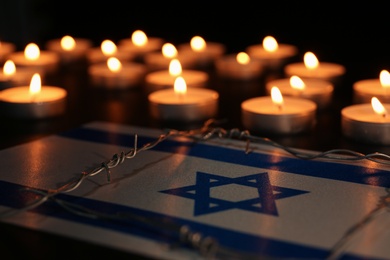 Photo of Flag of Israel, barbed wire and burning candles on black background. Holocaust memory day