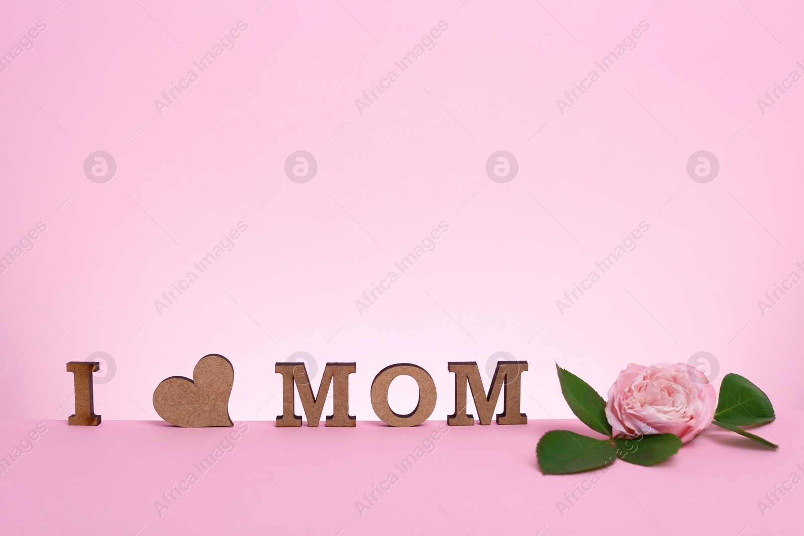 Photo of Phrase I LOVE MOM made of wooden letters with heart and flower for Mother's Day on color background