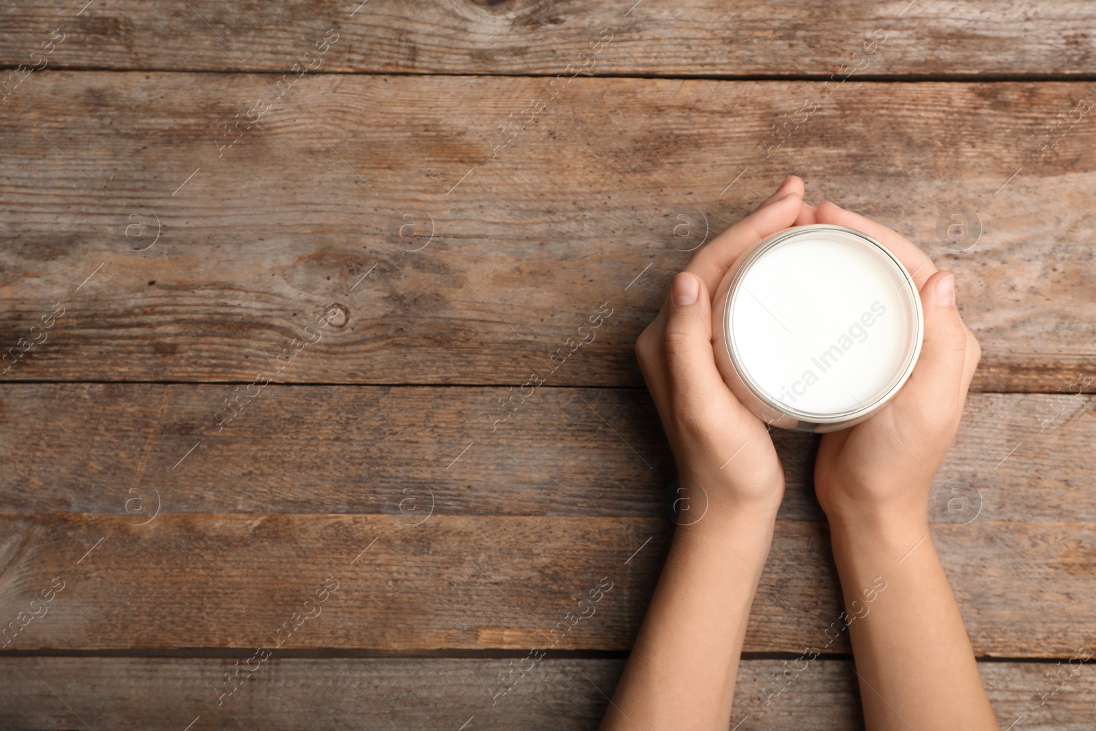 Photo of Woman holding glass of milk on wooden table, top view. Space for text