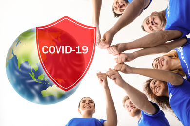Image of Volunteers uniting to help during COVID-19 outbreak. Group of people holing hands together on white background, shield and world globe illustrations