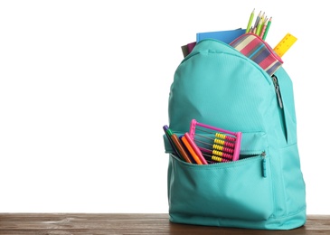 Stylish backpack with different school stationary on wooden table against white background