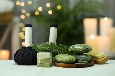 Photo of Spa composition. Herbal massage bags, stones and soap bars on white towel against blurred background