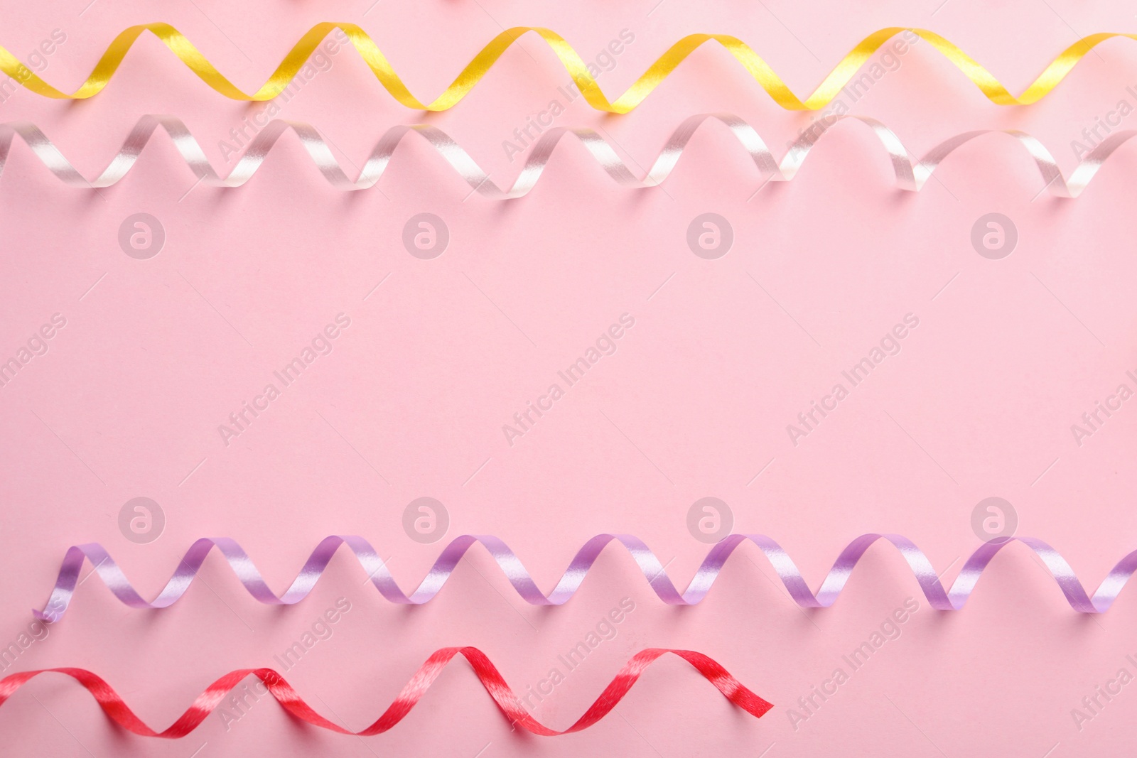 Photo of Colorful serpentine streamers on pink background, flat lay. Space for text