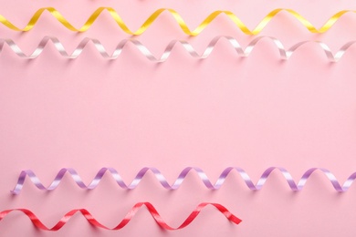 Colorful serpentine streamers on pink background, flat lay. Space for text