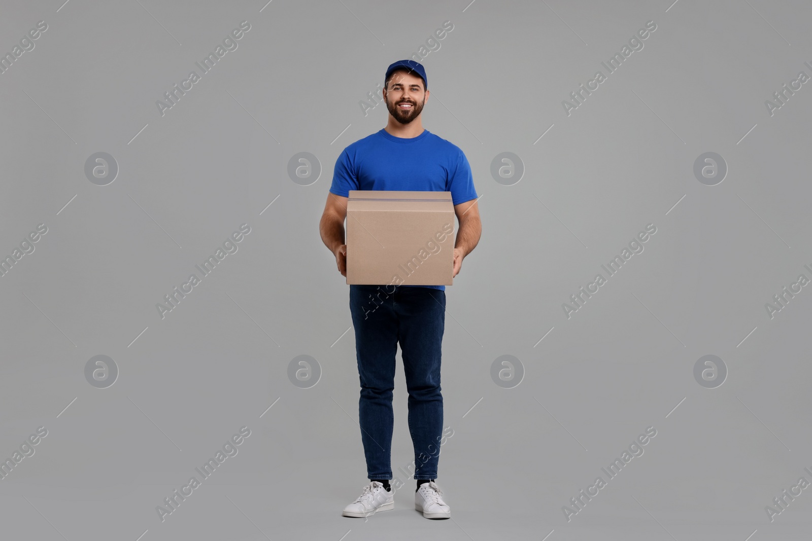 Photo of Happy young courier with parcel on grey background