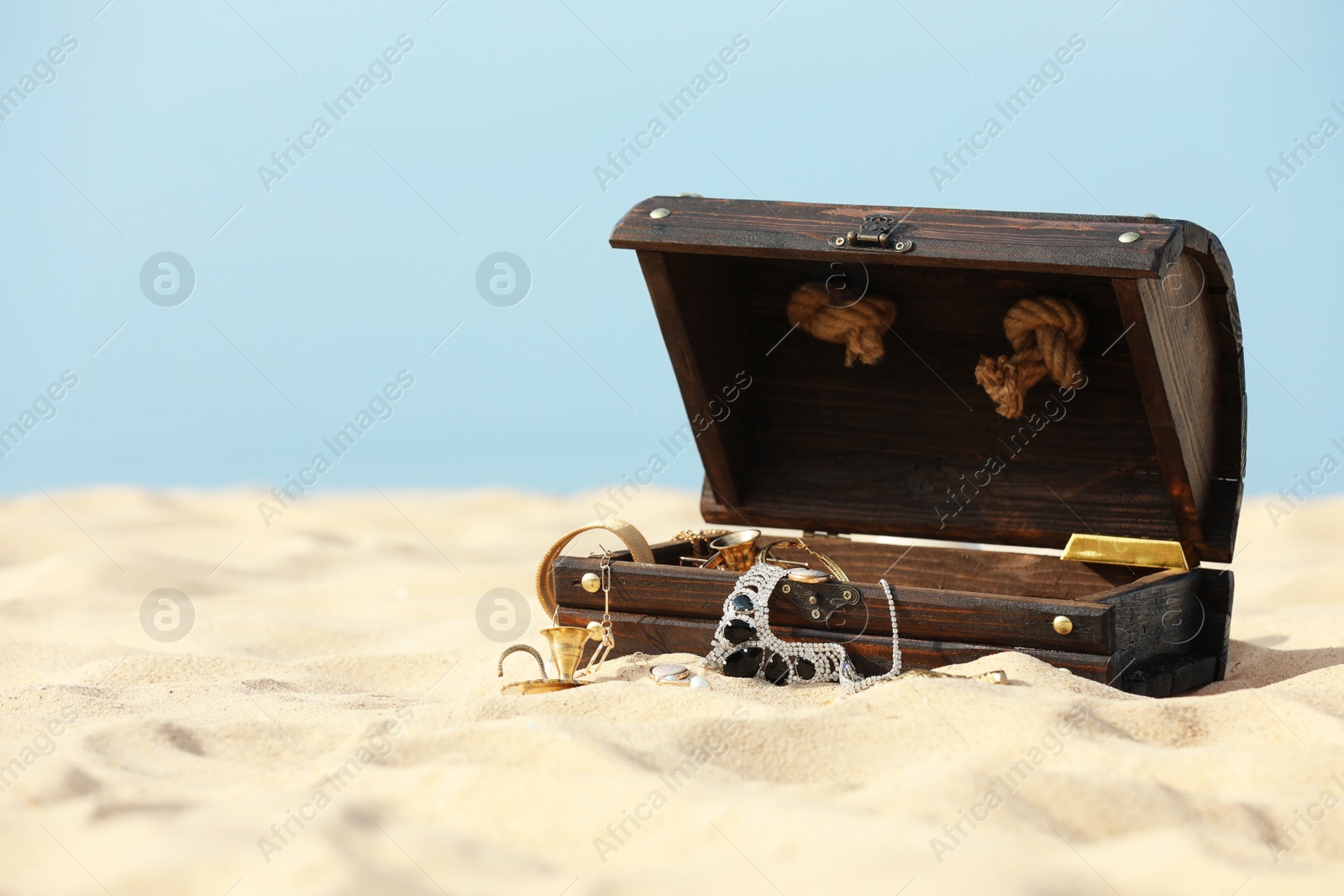 Photo of Open wooden chest with treasures on sandy beach, space for text