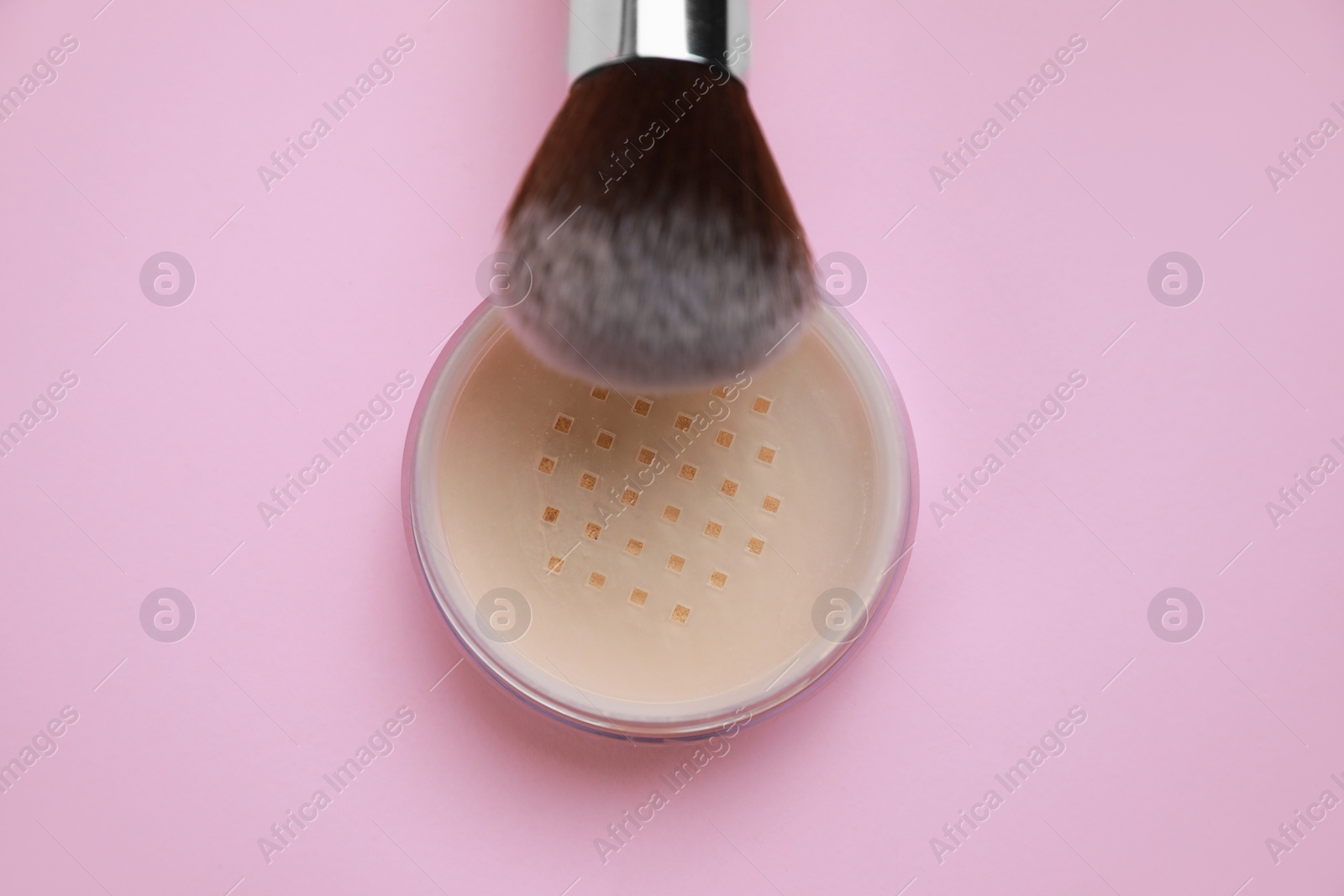 Photo of Loose face powder and brush on pink background, top view