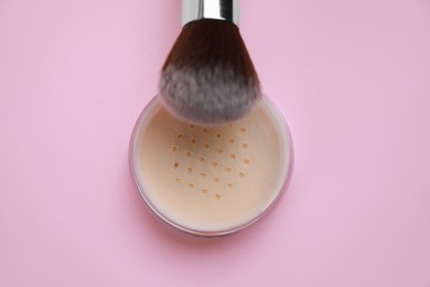 Loose face powder and brush on pink background, top view