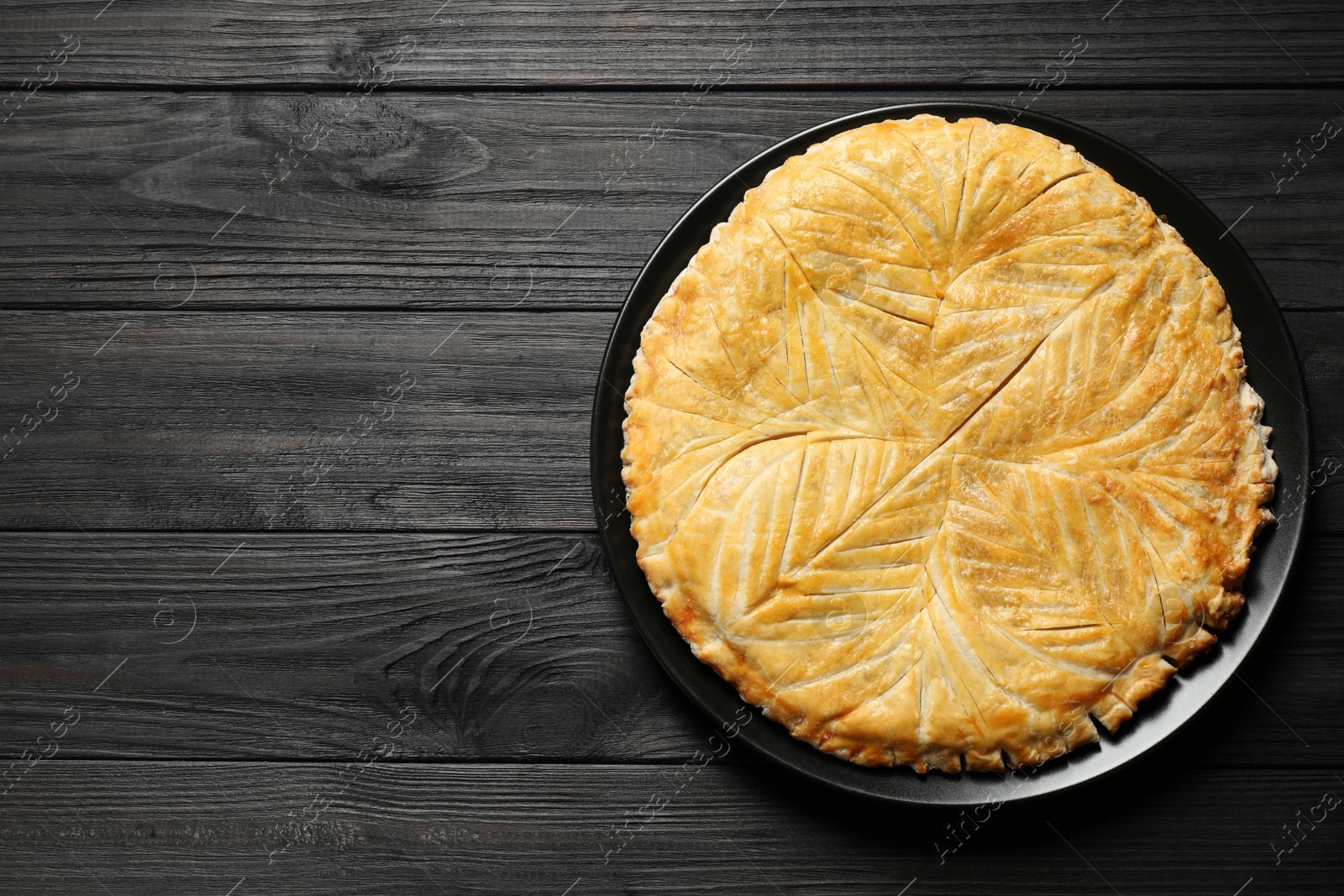 Photo of Traditional galette des rois on black wooden table, top view. Space for text