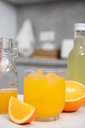 Tasty kombucha in glass, bottles and fresh orange on white table