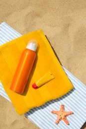 Photo of Sunscreen, lip balm, starfish and towels on sand, top view. Sun protection care