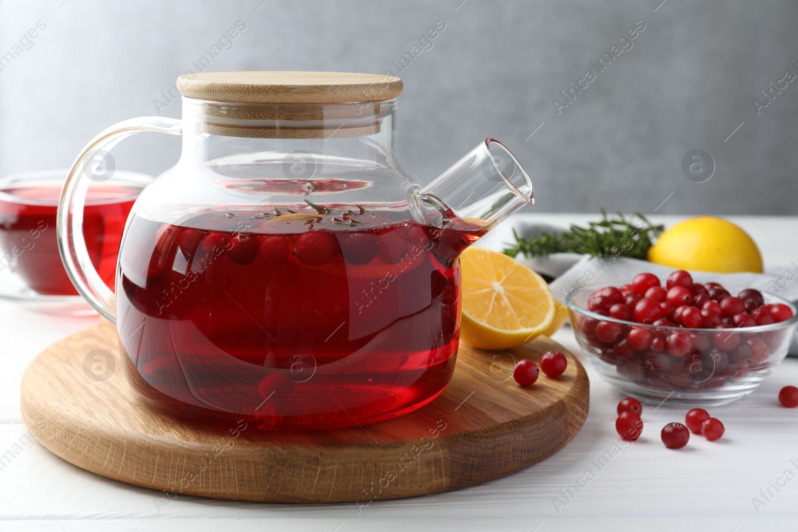 Photo of Tasty hot cranberry tea in teapot, lemon and fresh berries on white wooden table