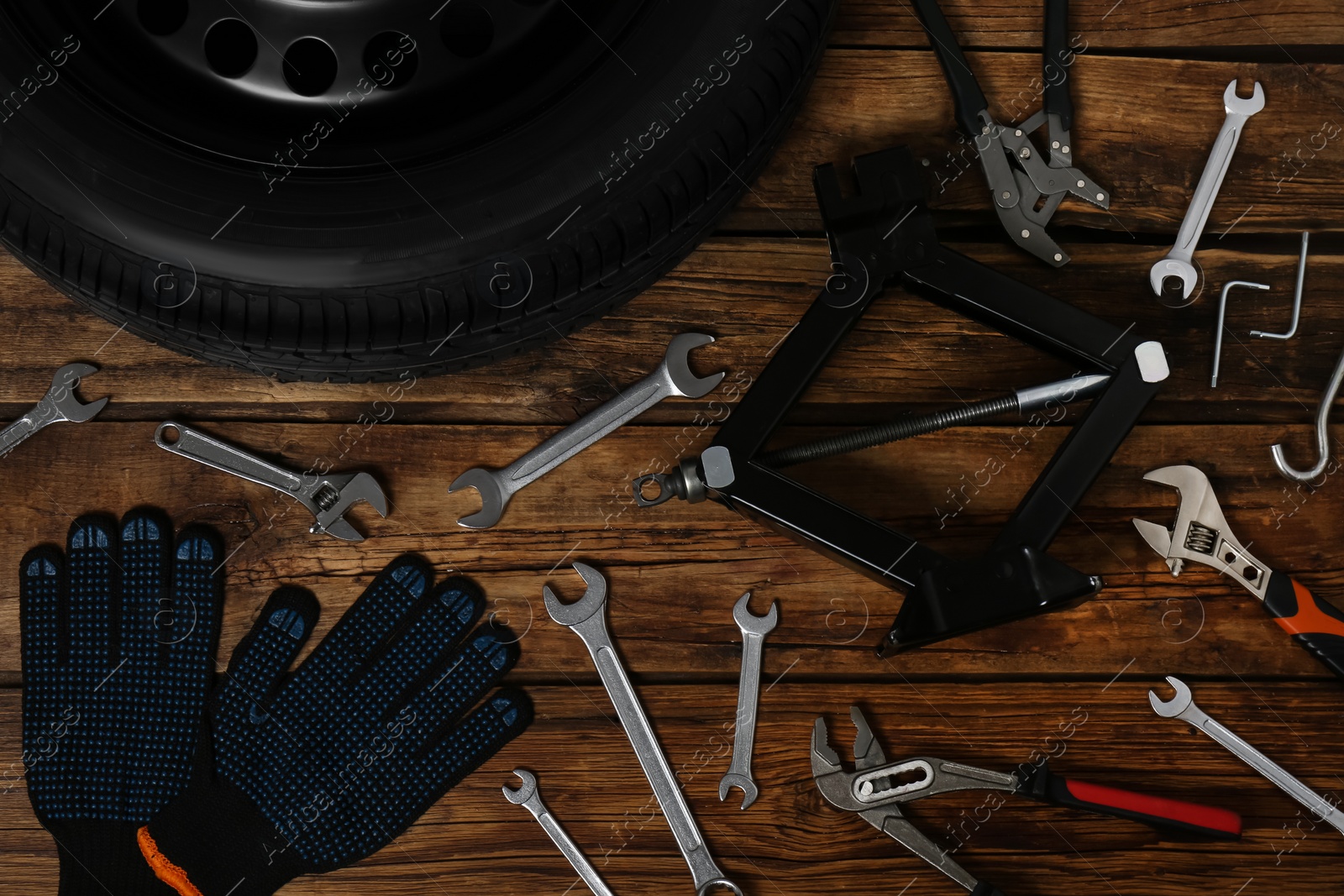 Photo of Car wheel, scissor jack, gloves and different tools on wooden surface, flat lay