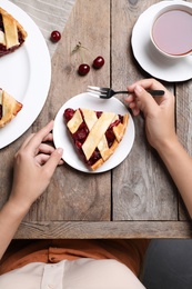 Photo of Woman eating delicious cherry pie at wooden table, top view