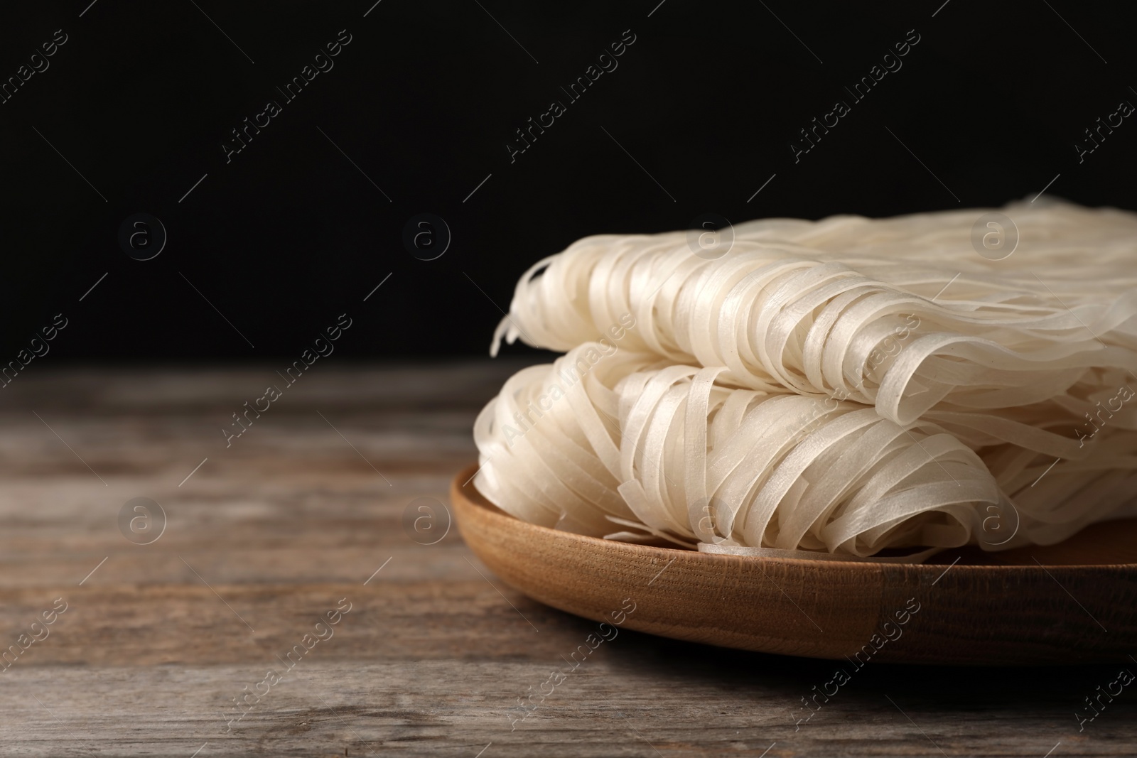 Photo of Plate with raw rice noodles on wooden table, closeup. Space for text