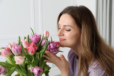 Photo of Woman smelling bouquet of beautiful tulips indoors