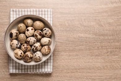 Photo of Bowl with quail eggs on wooden table, top view. Space for text