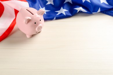 Photo of Piggy bank and American flag on white wooden table, space for text
