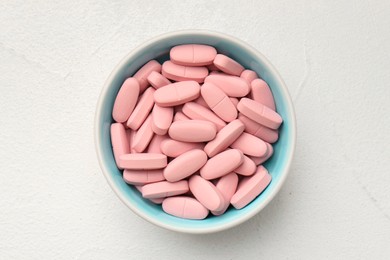 Vitamin capsules in bowl on white wooden table, top view