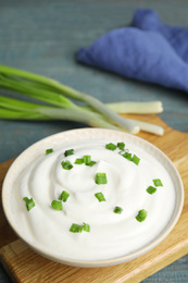 Photo of Fresh sour cream with onion on wooden board, closeup