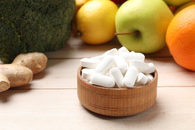 Photo of Dietary supplements. Bowl with pills near food products on light wooden table, closeup