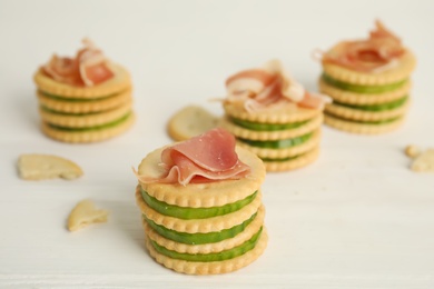 Photo of Delicious crackers with cucumber and prosciutto on white wooden table