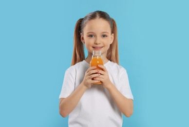 Photo of Cute little girl with bottle of fresh juice on light blue background