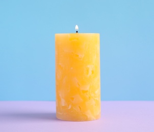 Alight scented wax candle on color background