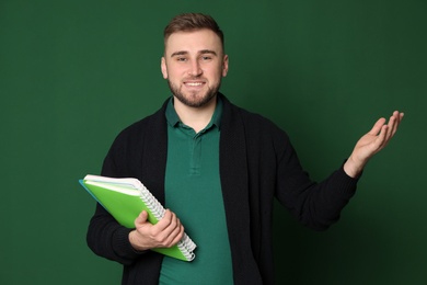 Portrait of young teacher with notebooks on green background