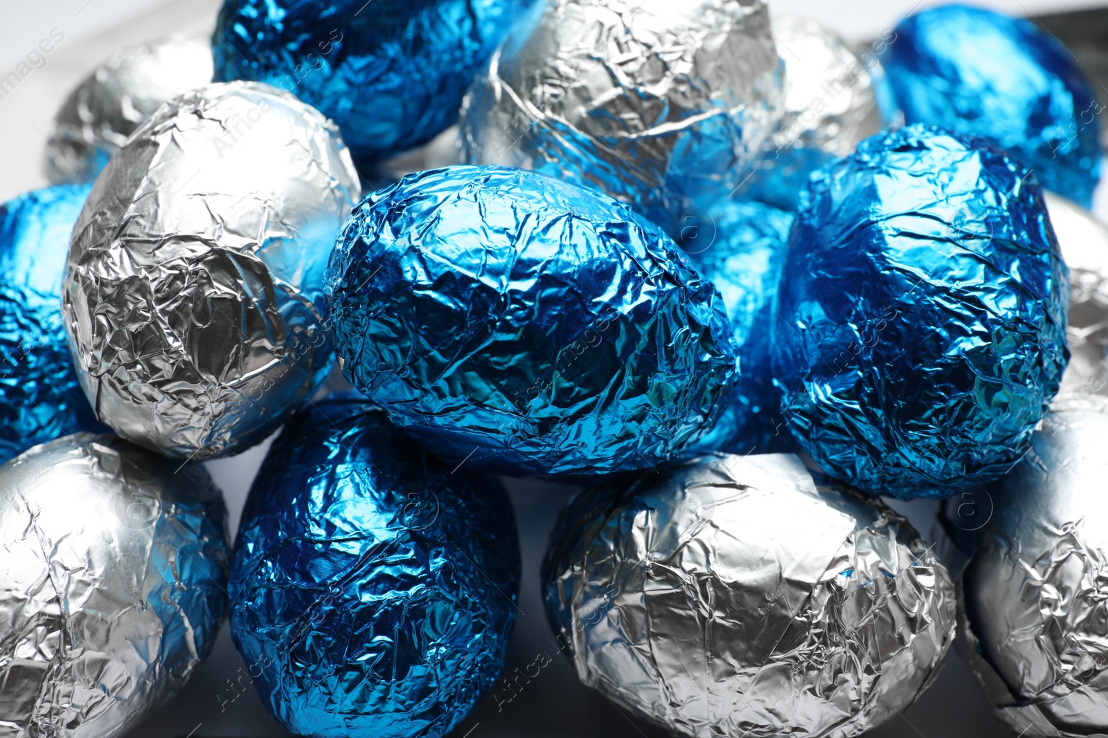 Photo of Chocolate eggs wrapped in blue and silver foil as background, closeup