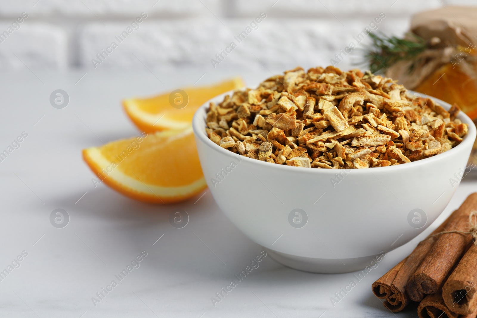 Photo of Bowl of dried orange zest seasoning, fresh fruit and cinnamon on white marble table. Space for text