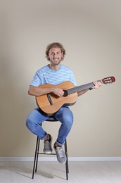 Photo of Young man playing acoustic guitar near grey wall
