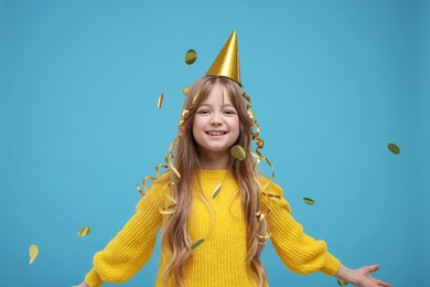 Photo of Happy little girl in party hat throwing confetti on light blue background