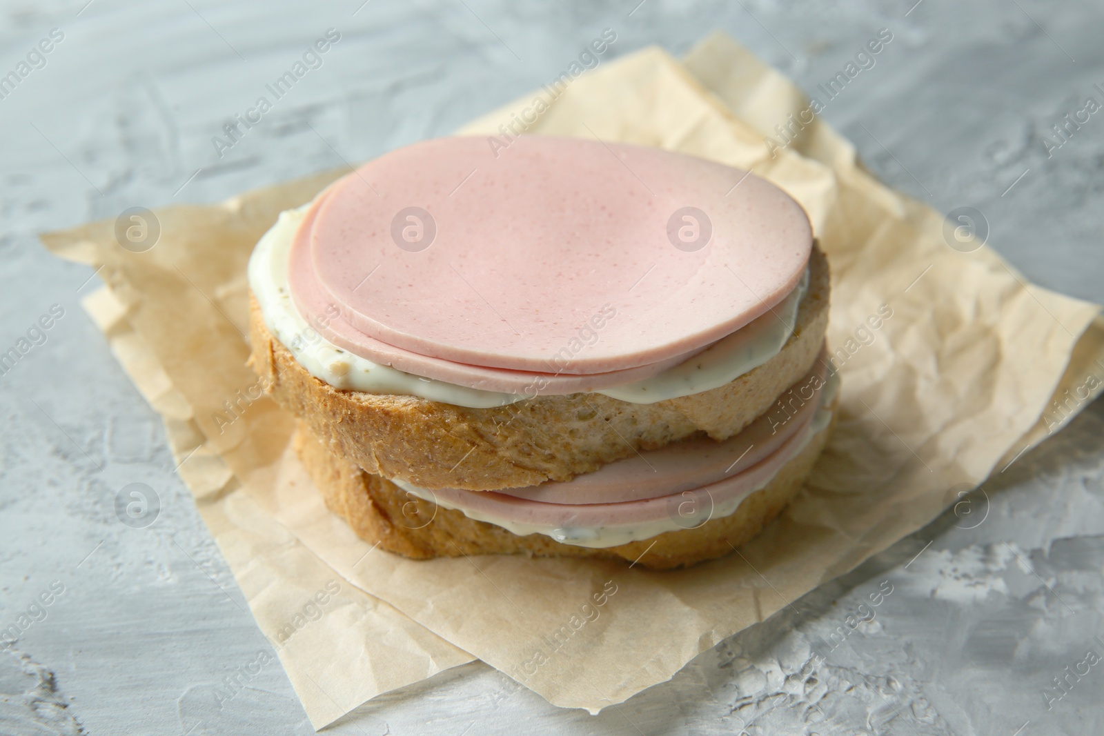 Photo of Delicious sandwich with boiled sausage and sauce on grey textured table, closeup