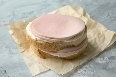 Delicious sandwich with boiled sausage and sauce on grey textured table, closeup