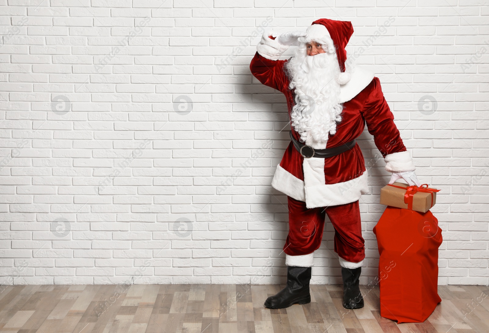 Photo of Authentic Santa Claus with bag full of gifts against white brick wall. Space for text