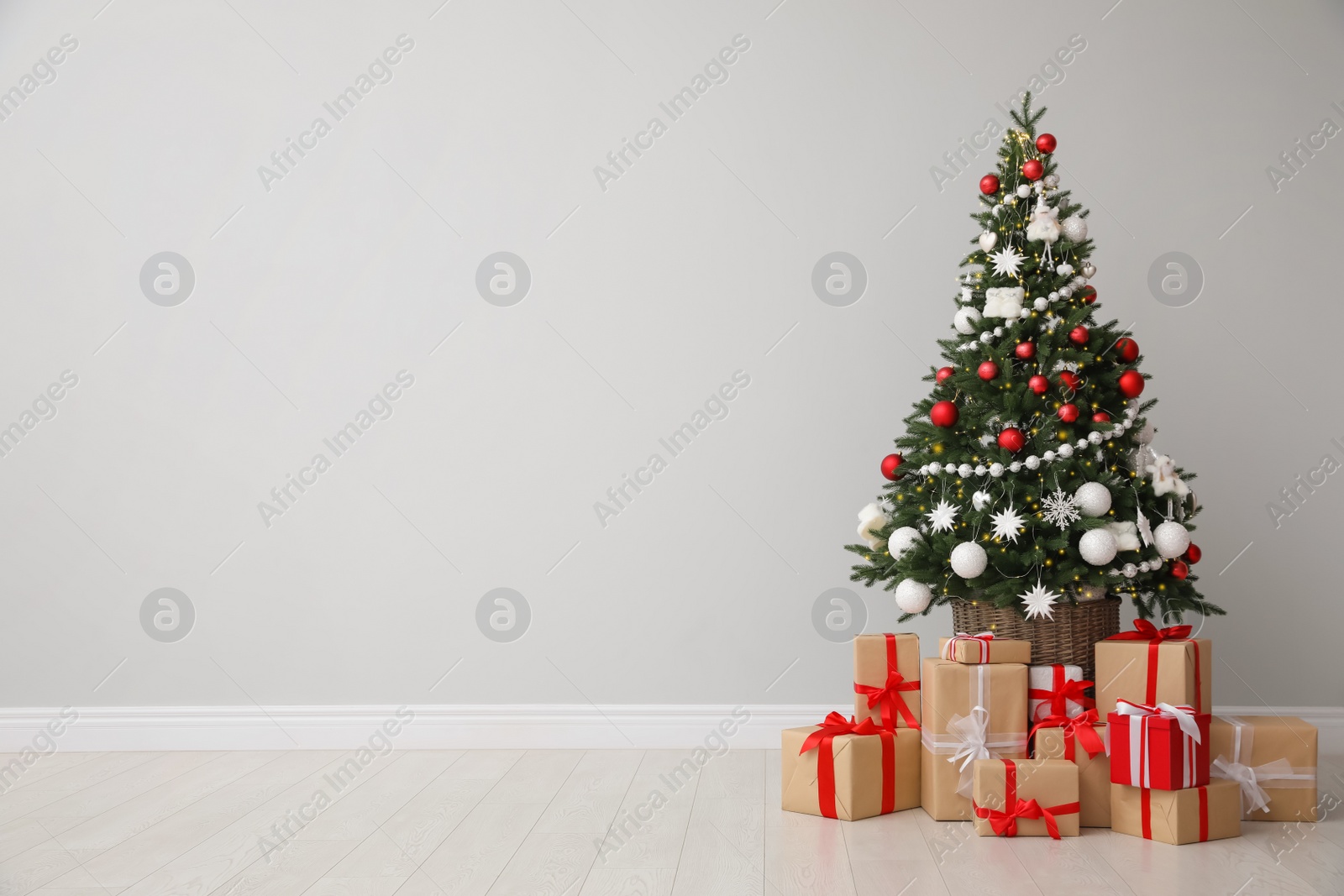 Photo of Christmas tree and gift boxes near light grey wall, space for text