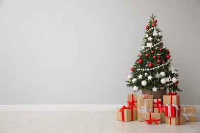 Photo of Christmas tree and gift boxes near light grey wall, space for text