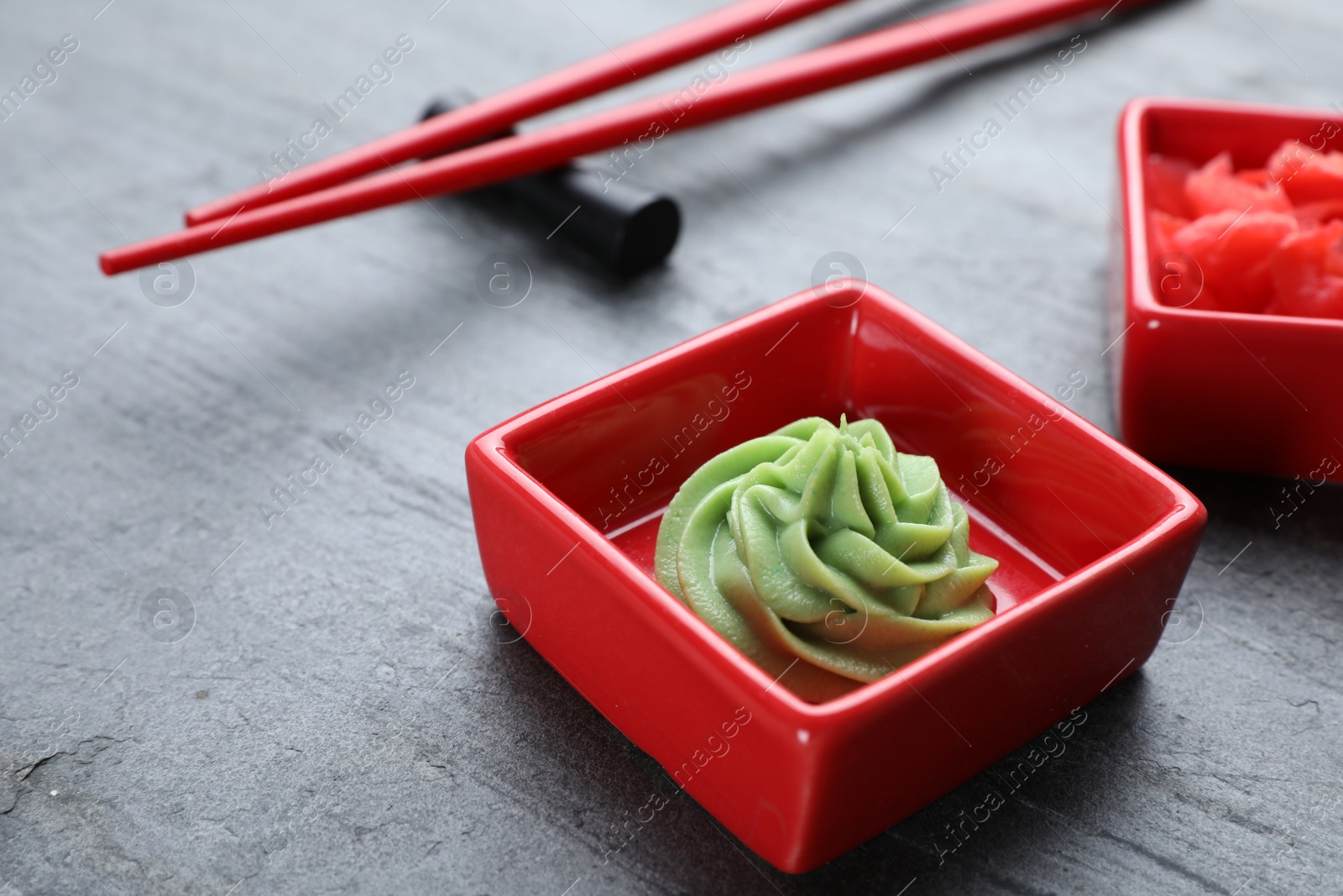 Photo of Bowls with swirl of wasabi paste and pickled ginger on grey table, closeup