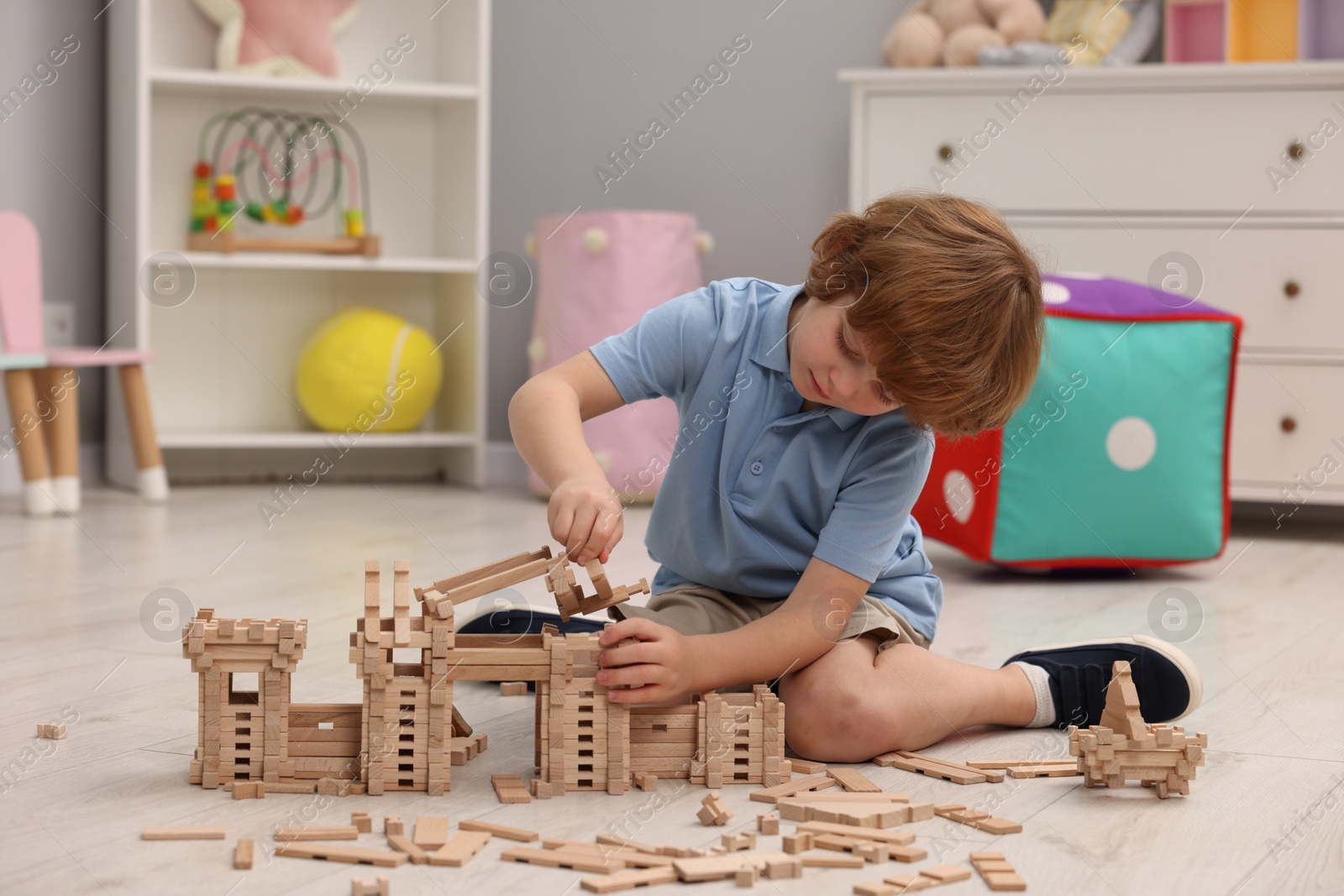 Photo of Little boy playing with wooden construction set on floor in room. Child's toy