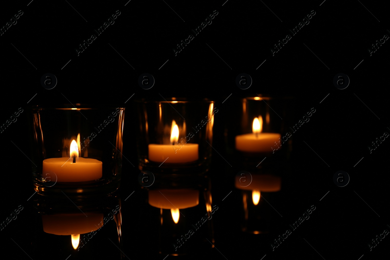 Photo of Burning candles in glass holders on table against dark background