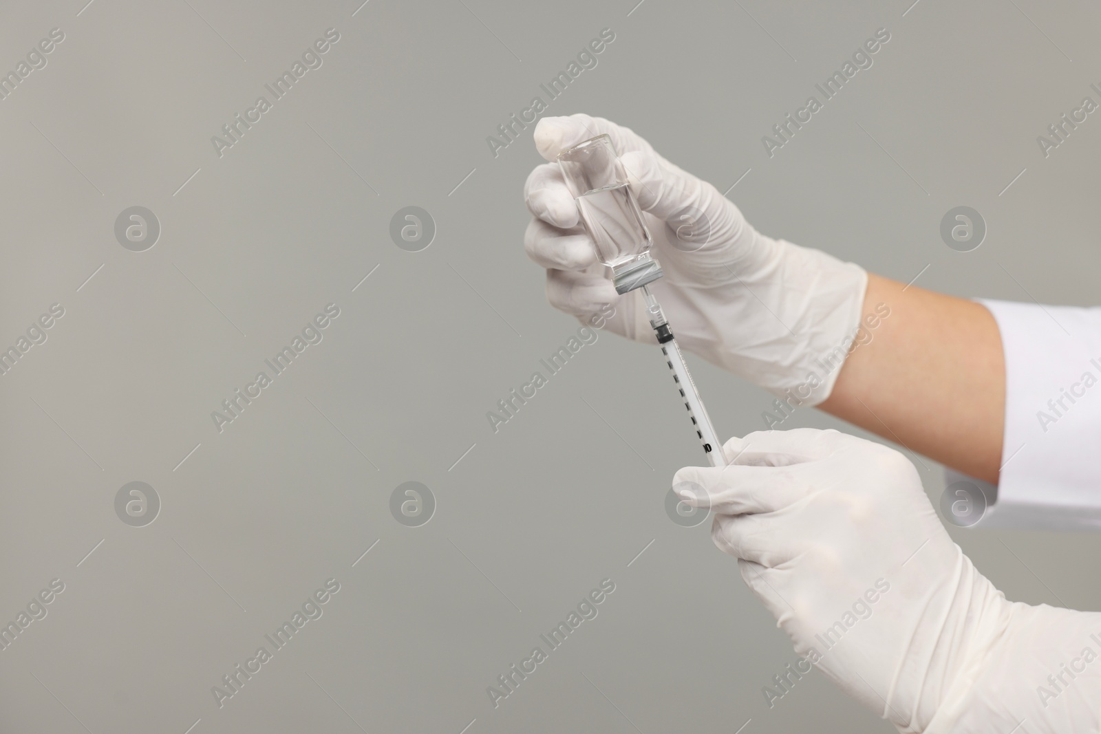 Photo of Doctor filling syringe with medication from glass vial on grey background, closeup. Space for text