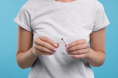 Photo of Stop smoking concept. Woman breaking cigarette on light blue background, closeup