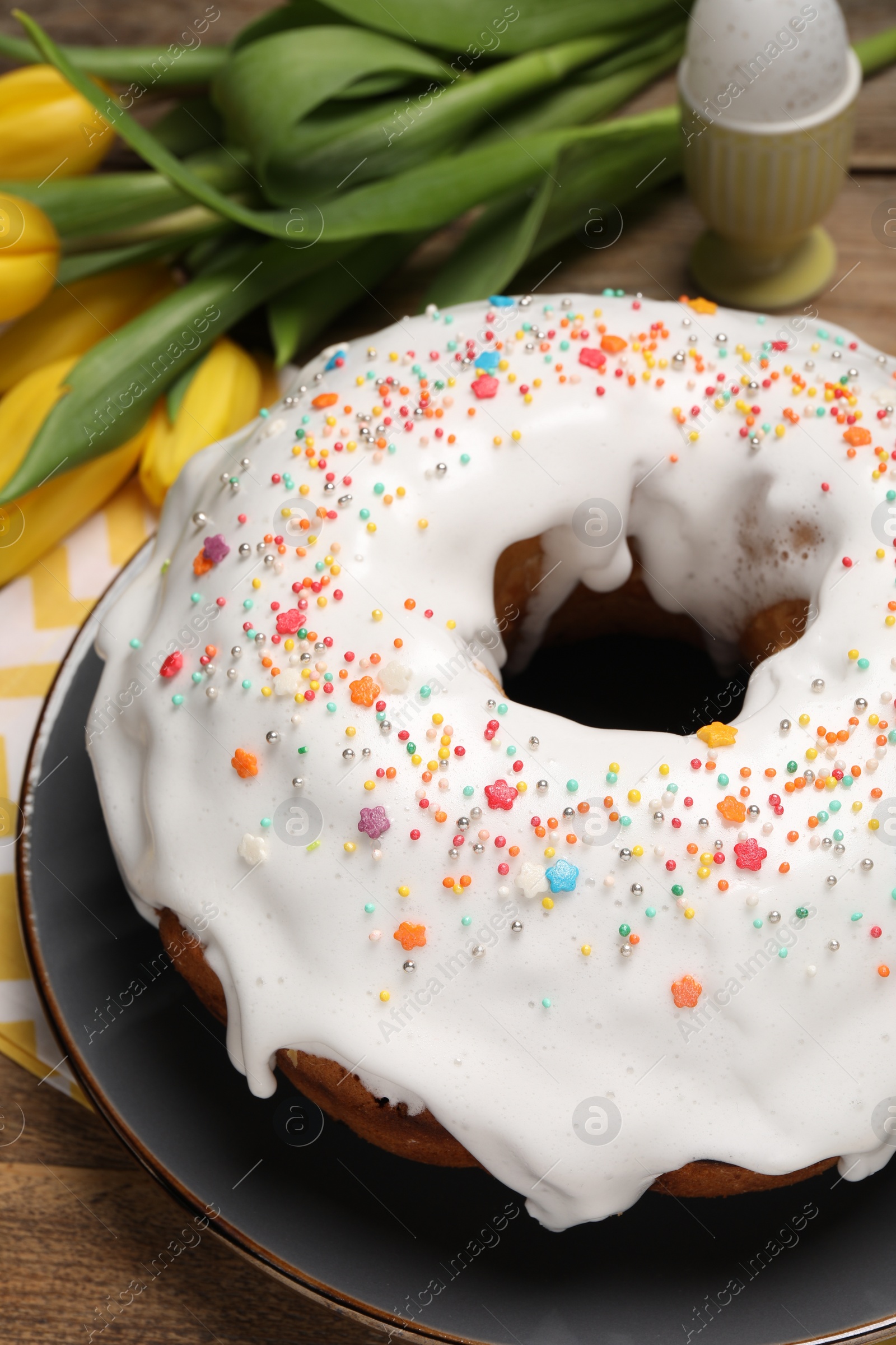 Photo of Easter cake with sprinkles and tulips on wooden table, closeup