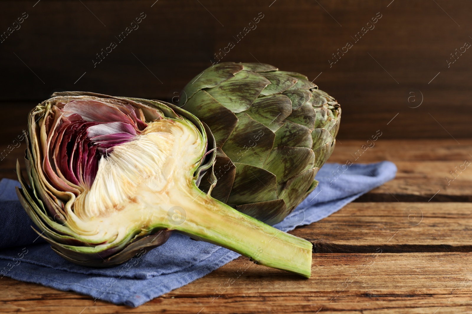 Photo of Cut and whole fresh raw artichokes on wooden table