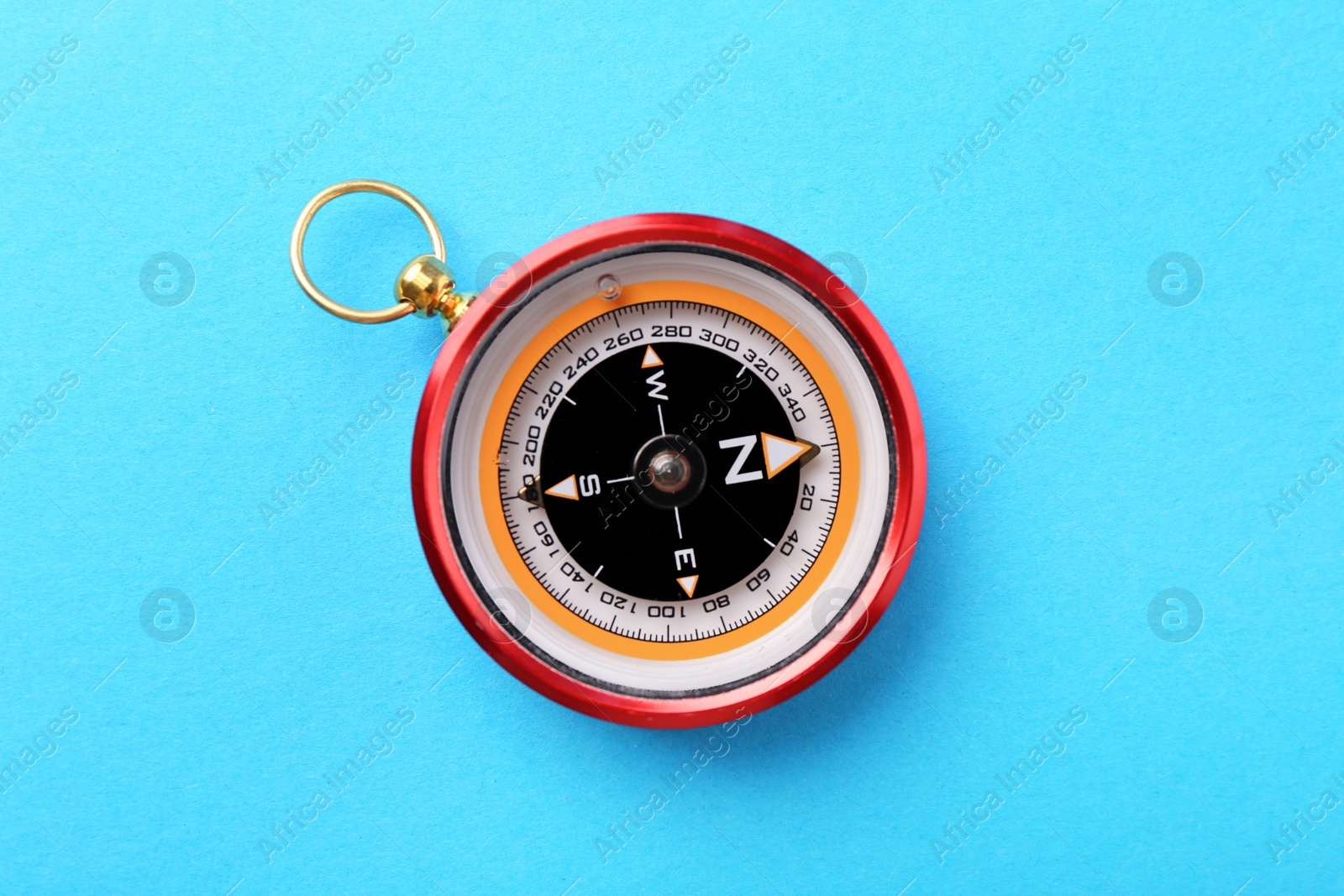 Photo of Compass on light blue background, top view. Navigation equipment