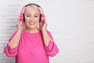 Mature woman enjoying music in headphones against brick wall. Space for text