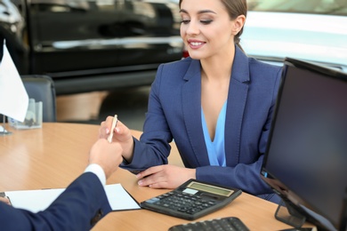 Photo of Young woman signing documents in car salon
