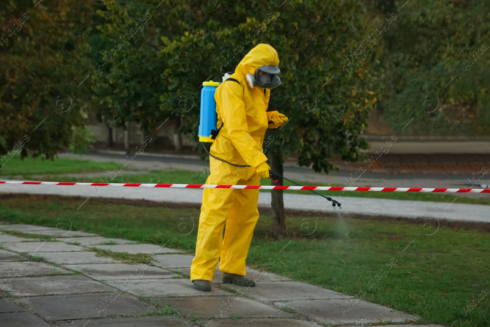 Photo of Person in hazmat suit disinfecting street pavement with sprayer. Surface treatment during coronavirus pandemic