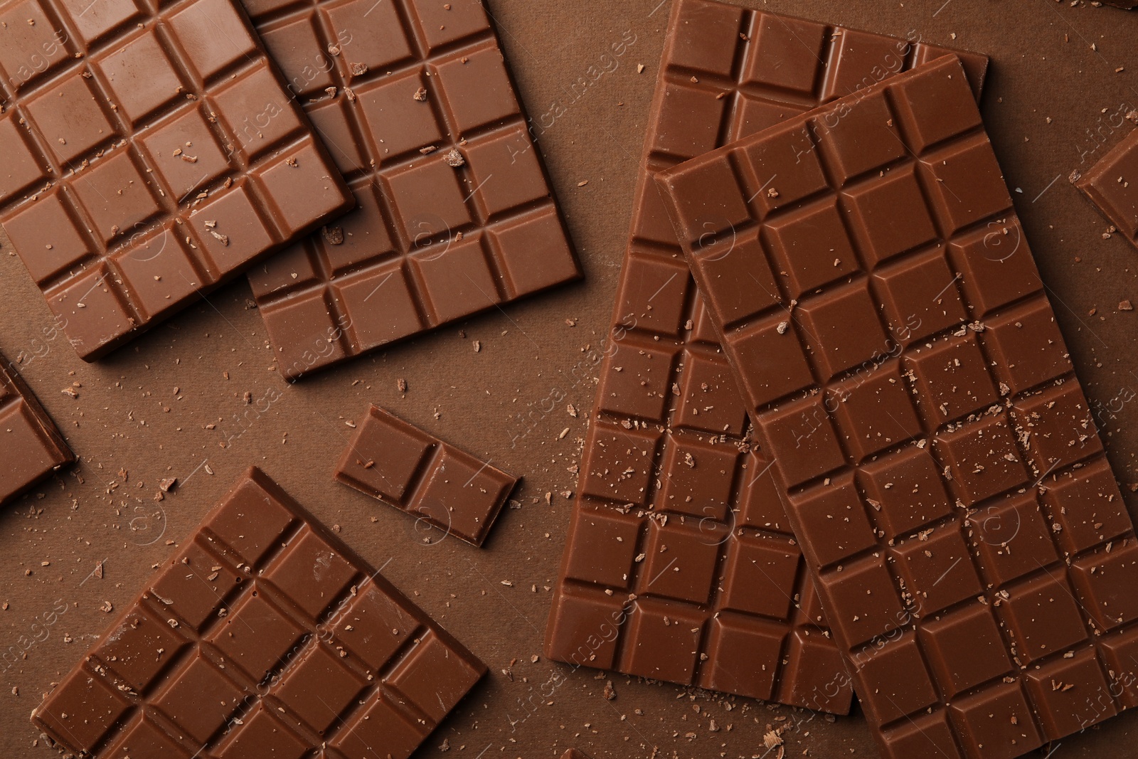 Photo of Pieces of tasty chocolate on brown background, flat lay